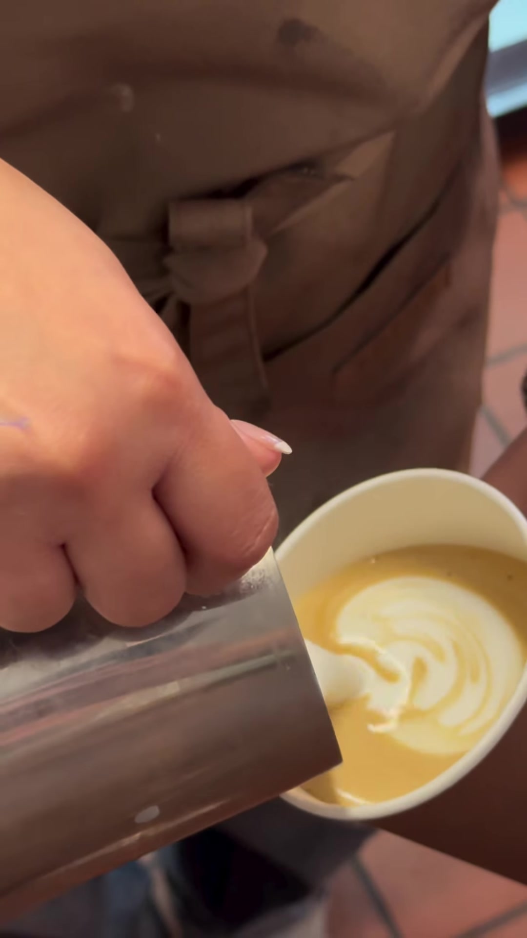 Hands carefully pouring latte art into a Sahara coffee cup